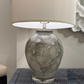 Table lamp with textured glass base and beige shade on a textured surface.