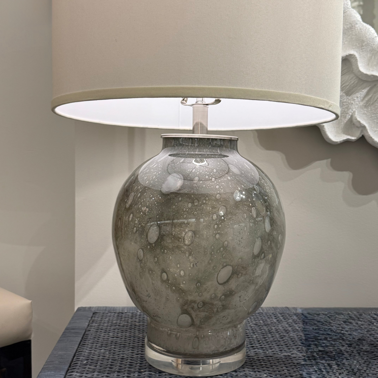 Table lamp with textured glass base and beige shade on a textured surface.