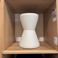 White cylindrical object on a wooden shelf with a brown leather item above