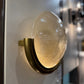 Decorative wall light fixture with textured glass shade and brass fixture on a white wall.