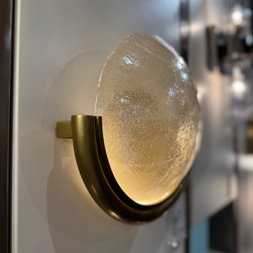 Decorative wall light fixture with textured glass shade and brass fixture on a white wall.