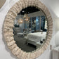 Round mirror with decorative beige frame on a white wall
