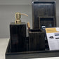 Bathroom vanity set with black marble tray, gold pump, and other accessories on a white counter.