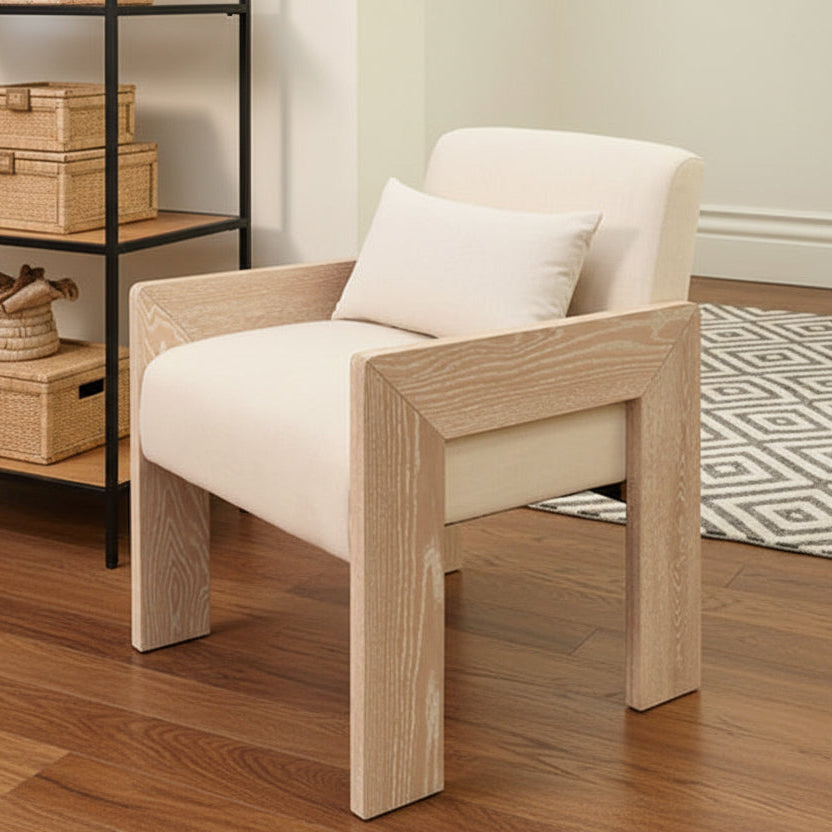 Beige armchair with wooden legs in a room with a shelf and rug.
