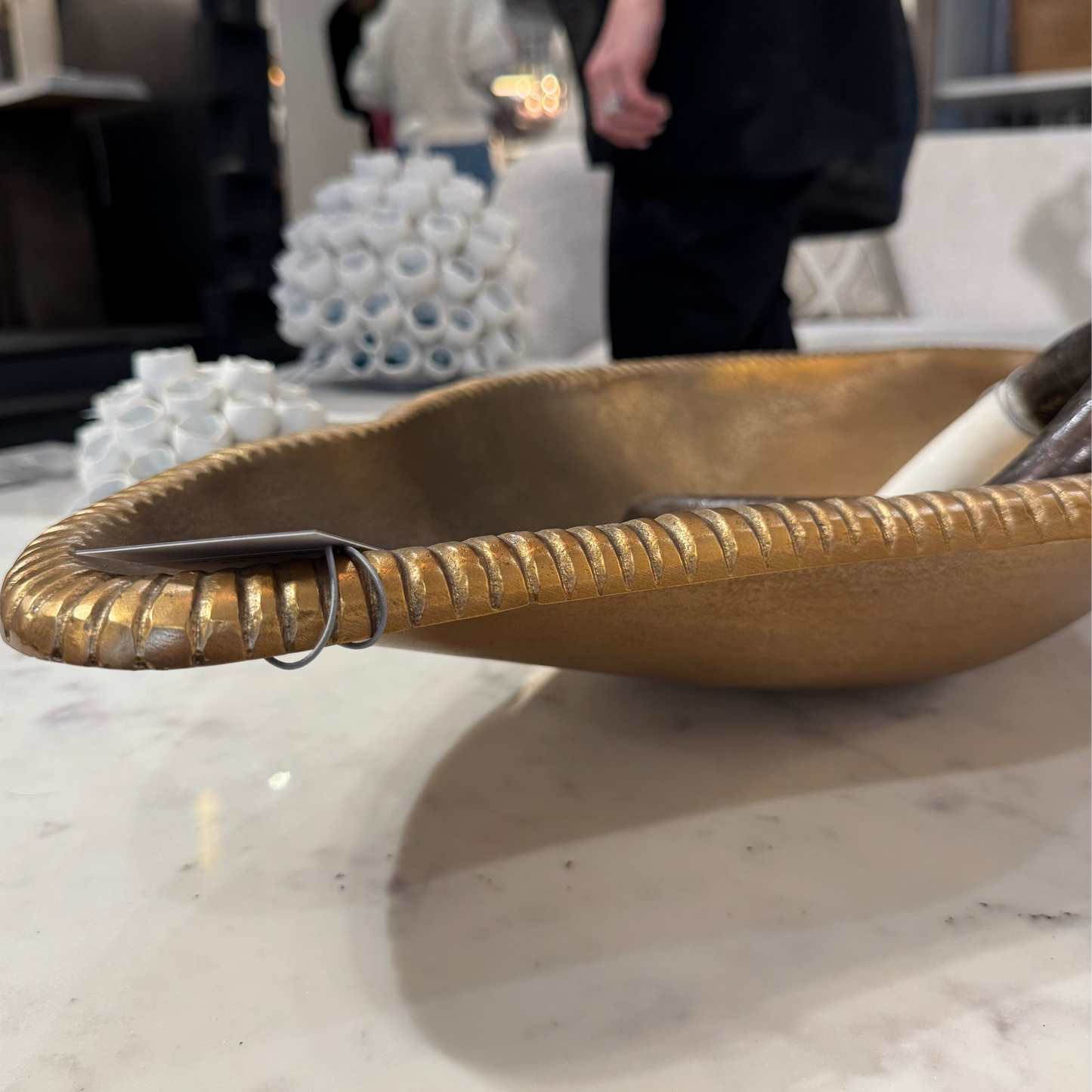 Gold decorative bowl on a marble surface with blurred people in the background