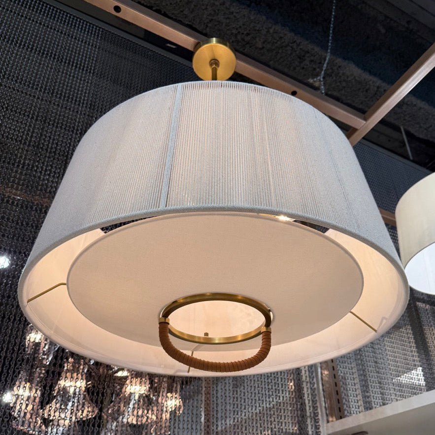 Large pendant light with a white shade and gold fixture hanging in a showroom.