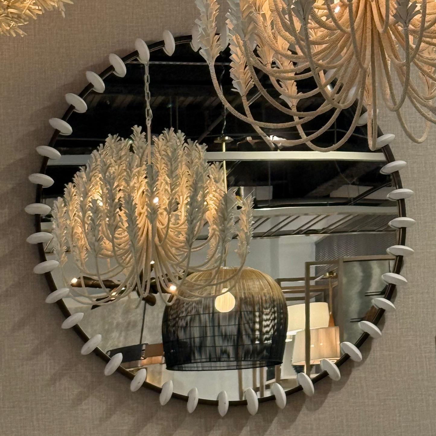 Decorative mirror with a chandelier reflection on a beige wall.