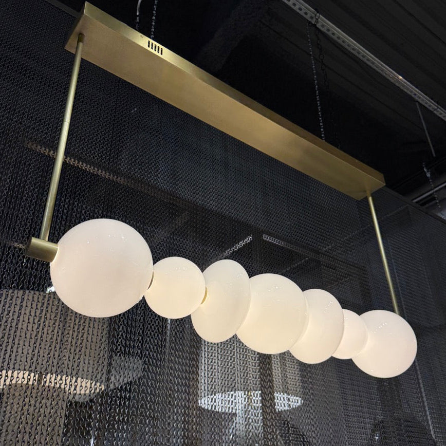 Chandelier with round glass shades hanging from a gold frame against a dark ceiling.