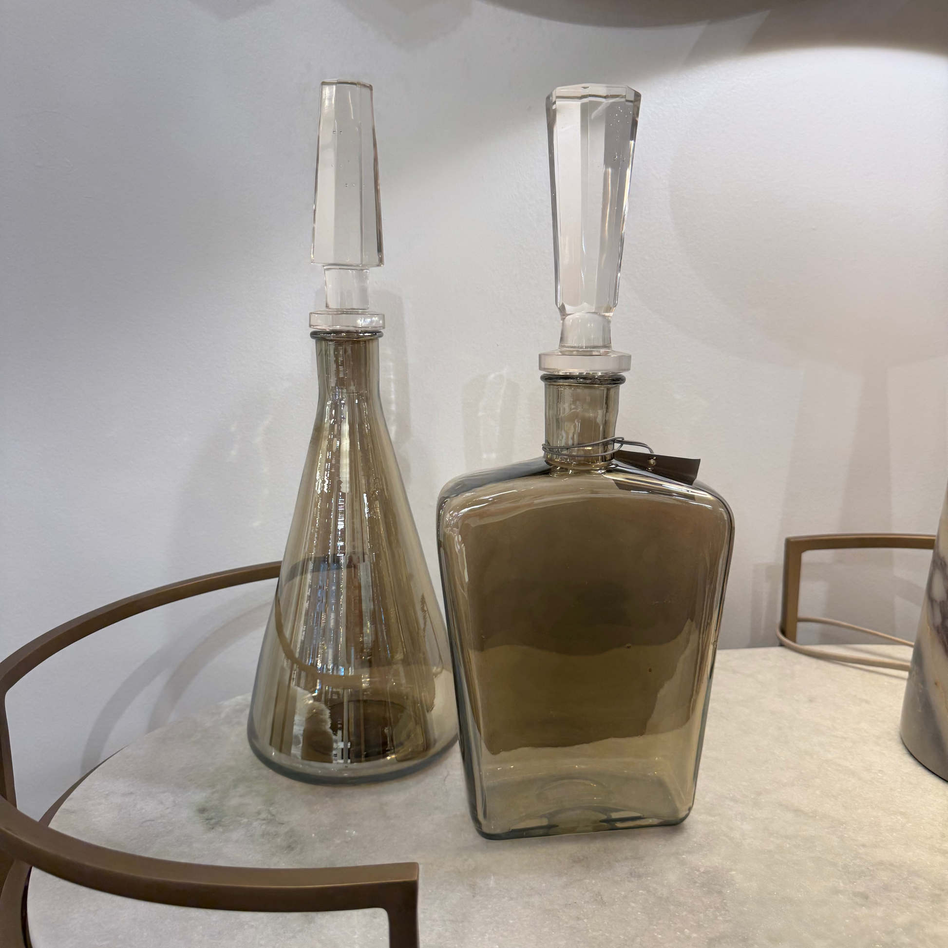Two glass bottles on a marble surface with a white wall in the background