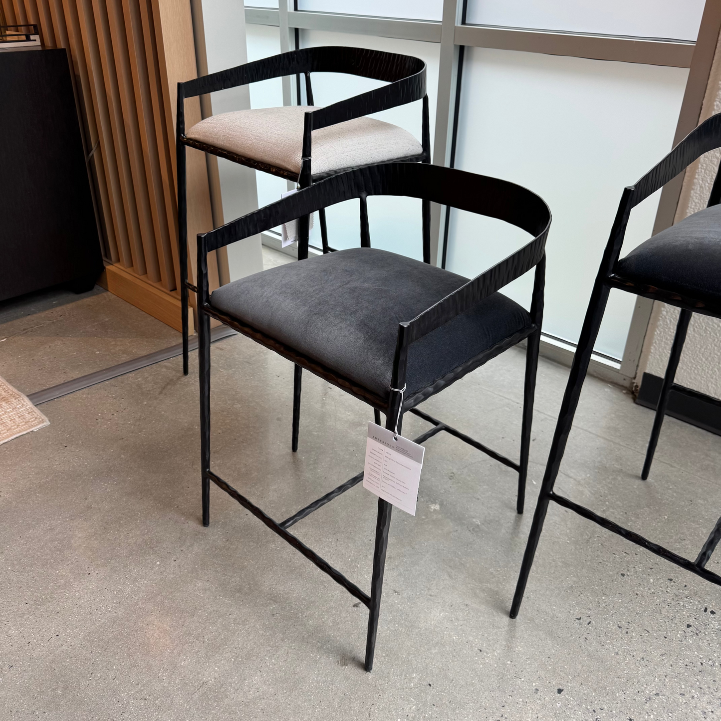 Modern black bar stools with gray seats in a showroom setting.