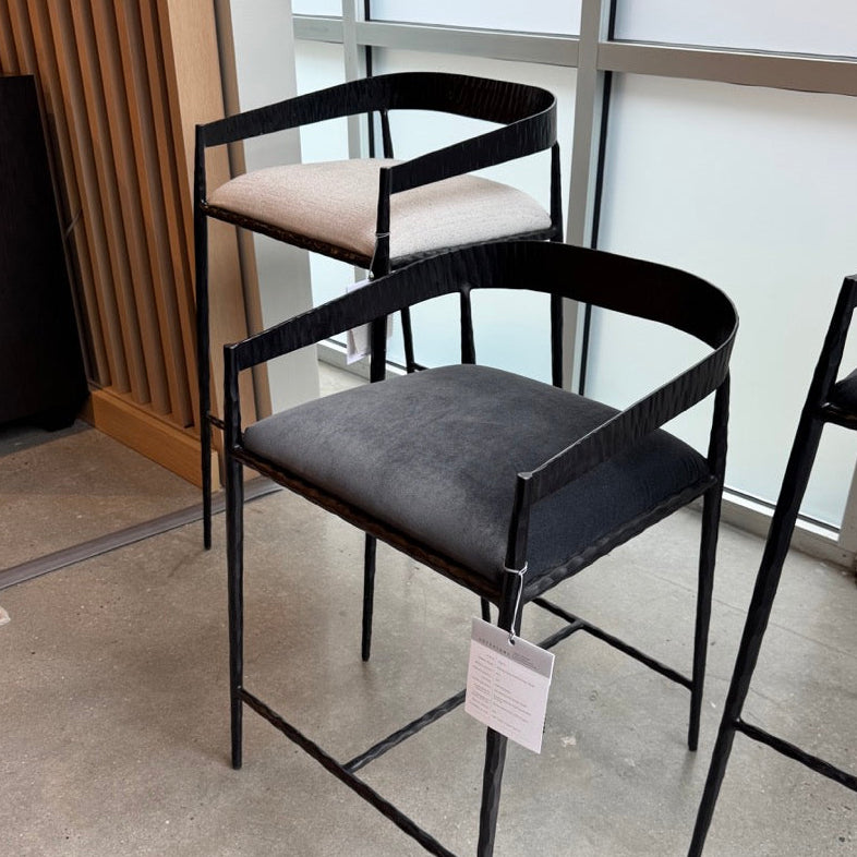 Black metal bar stools with gray cushioned seats in a showroom setting.