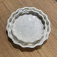 Set of three white ceramic bowls with scalloped edges on a textured surface