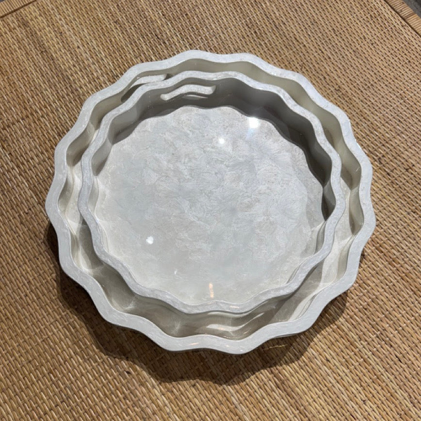 Set of three white ceramic bowls with scalloped edges on a textured surface