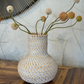 Woven vase with decorative flowers on a wooden surface with a textured wall background