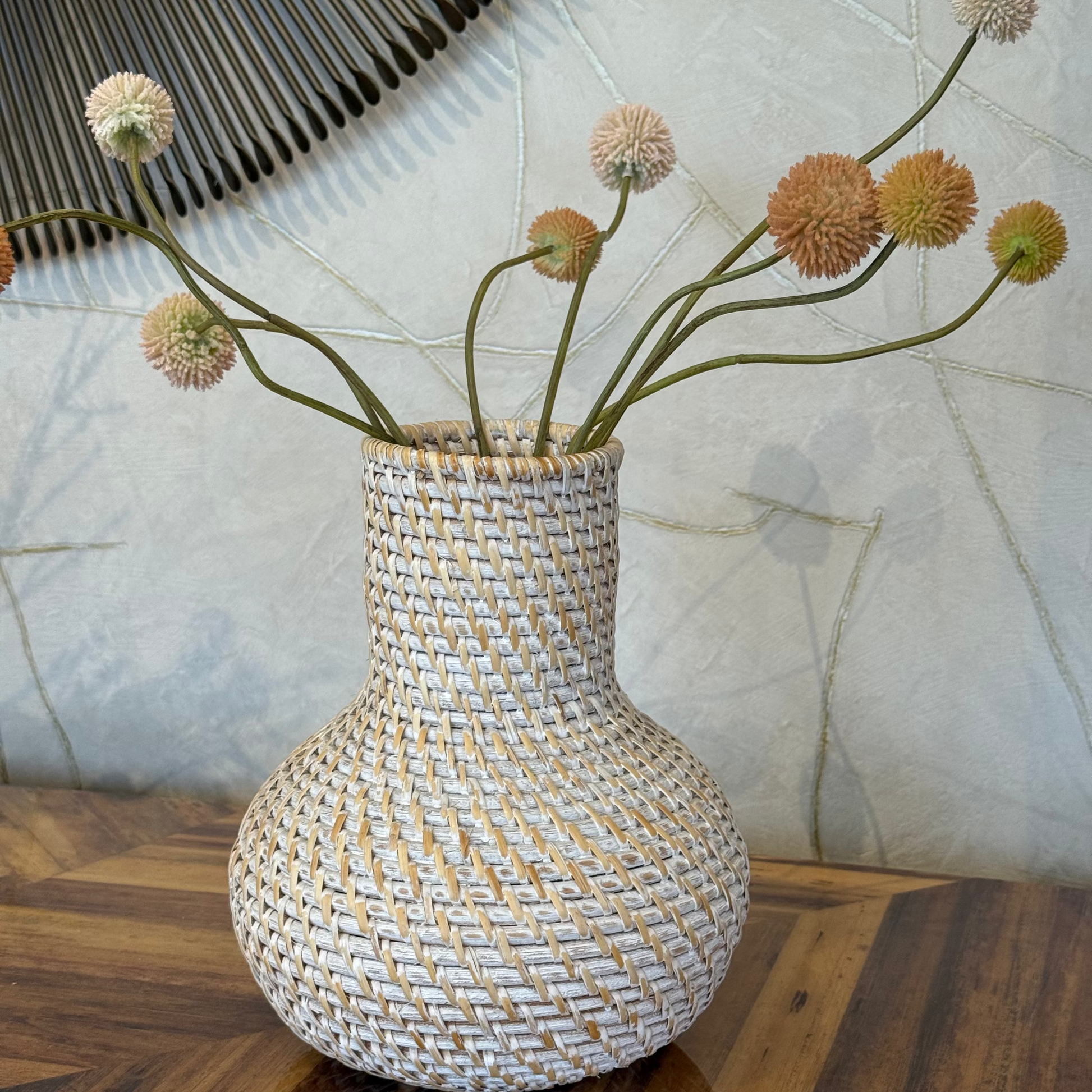 Woven vase with decorative flowers on a wooden surface with a textured wall background