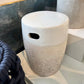 White and gray textured vase on a surface with a mirror and decorative item in the background