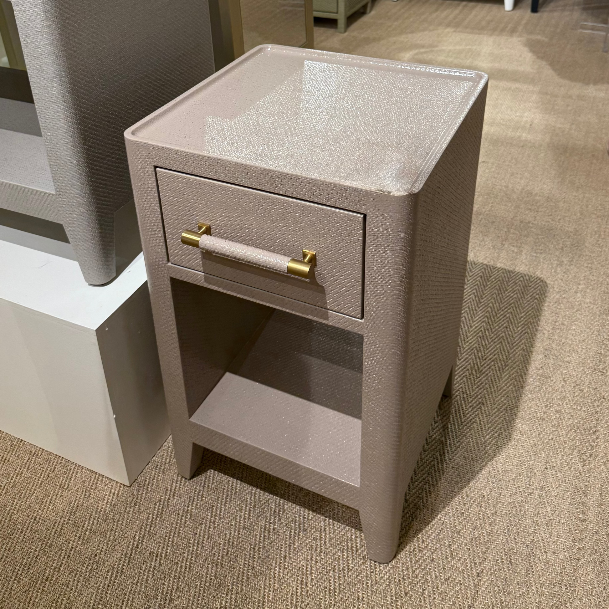 Beige textured nightstand with gold handles in a showroom setting