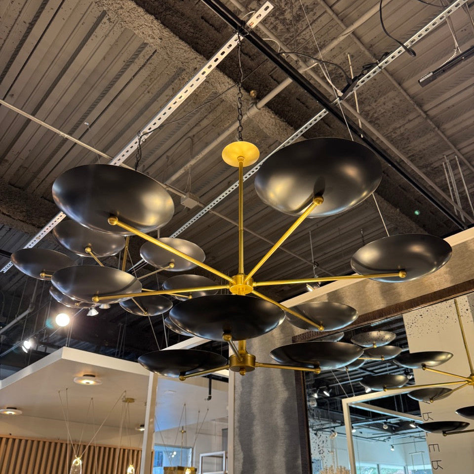 Modern chandelier with black lampshades and gold fixture in a showroom setting.