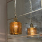Gold pendant light hanging in front of a mirror on a concrete wall.