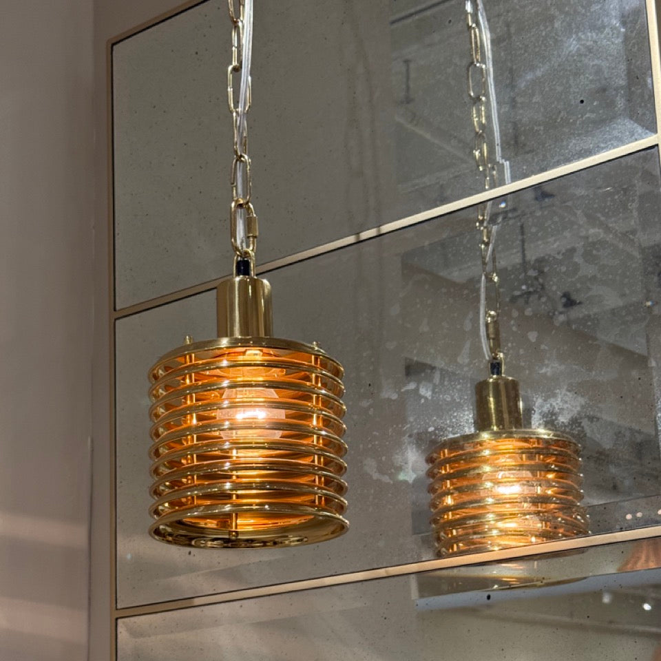 Gold pendant light hanging in front of a mirror on a concrete wall.