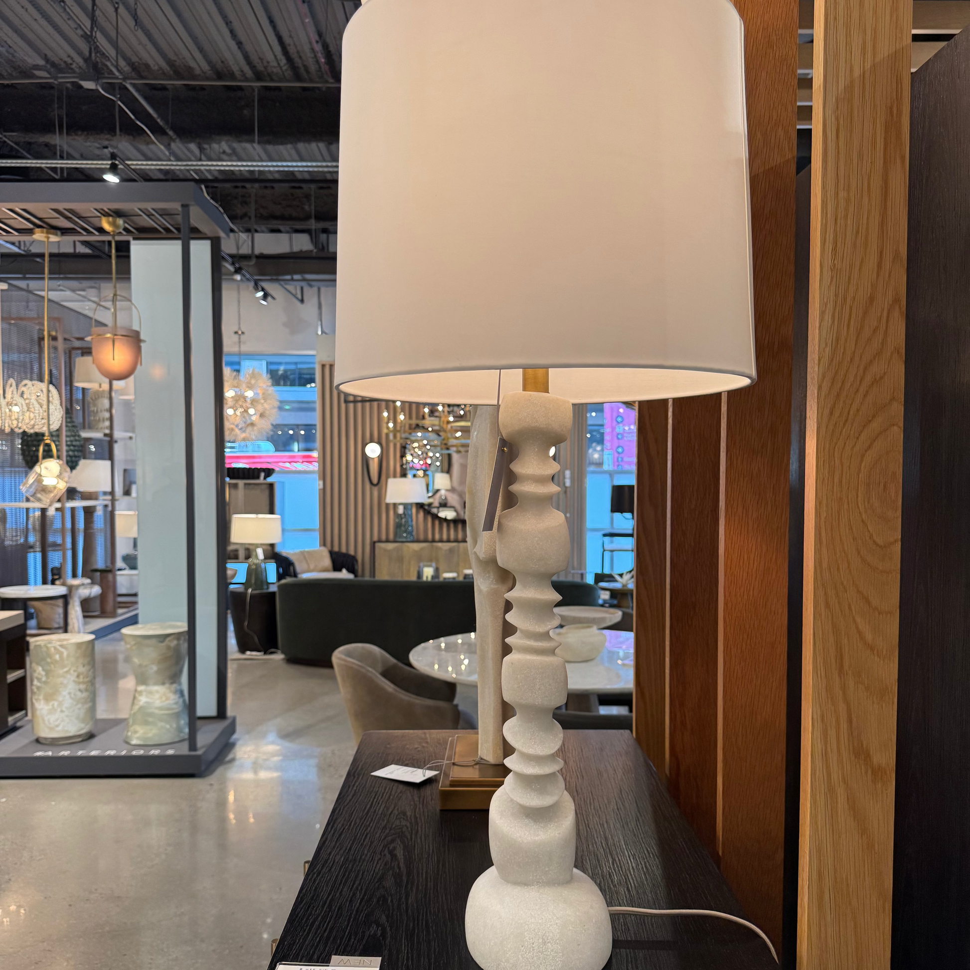 White table lamp with a beige shade on a black surface in a showroom setting.