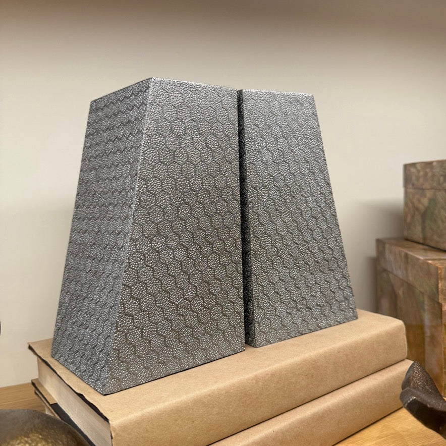 Two gray textured bookends on a cardboard box with a wooden surface and light-colored wall in the background.