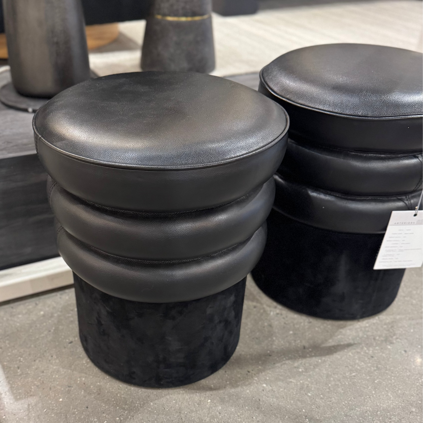 Black cushioned stools on a concrete floor with a blurred background
