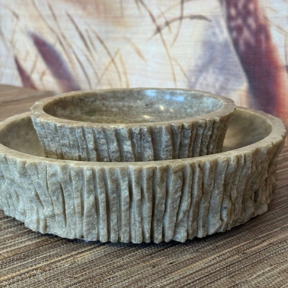 Set of two textured stone bowls on a striped surface with a blurred background