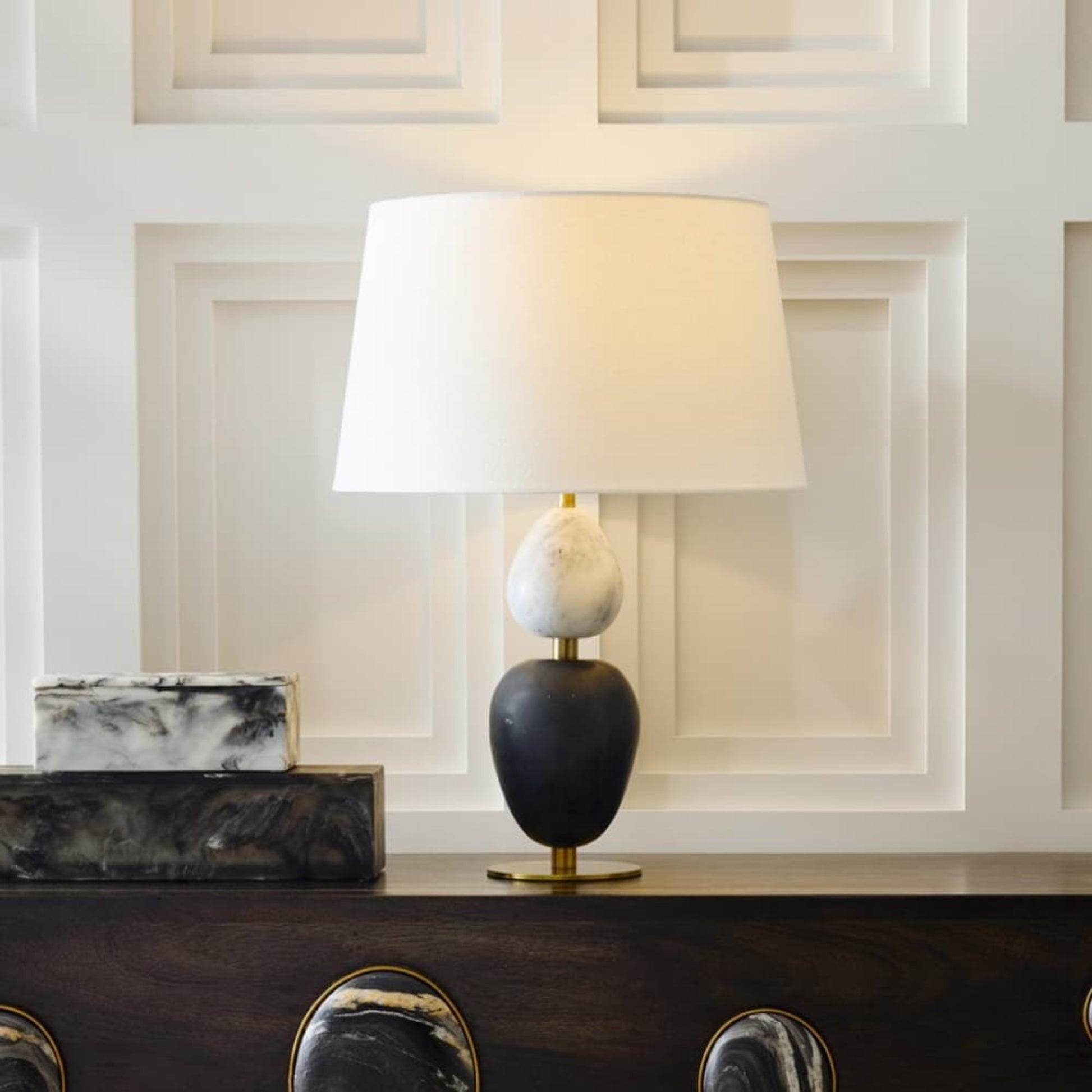 Decorative table lamp with marble base on a wooden surface against a paneled wall.