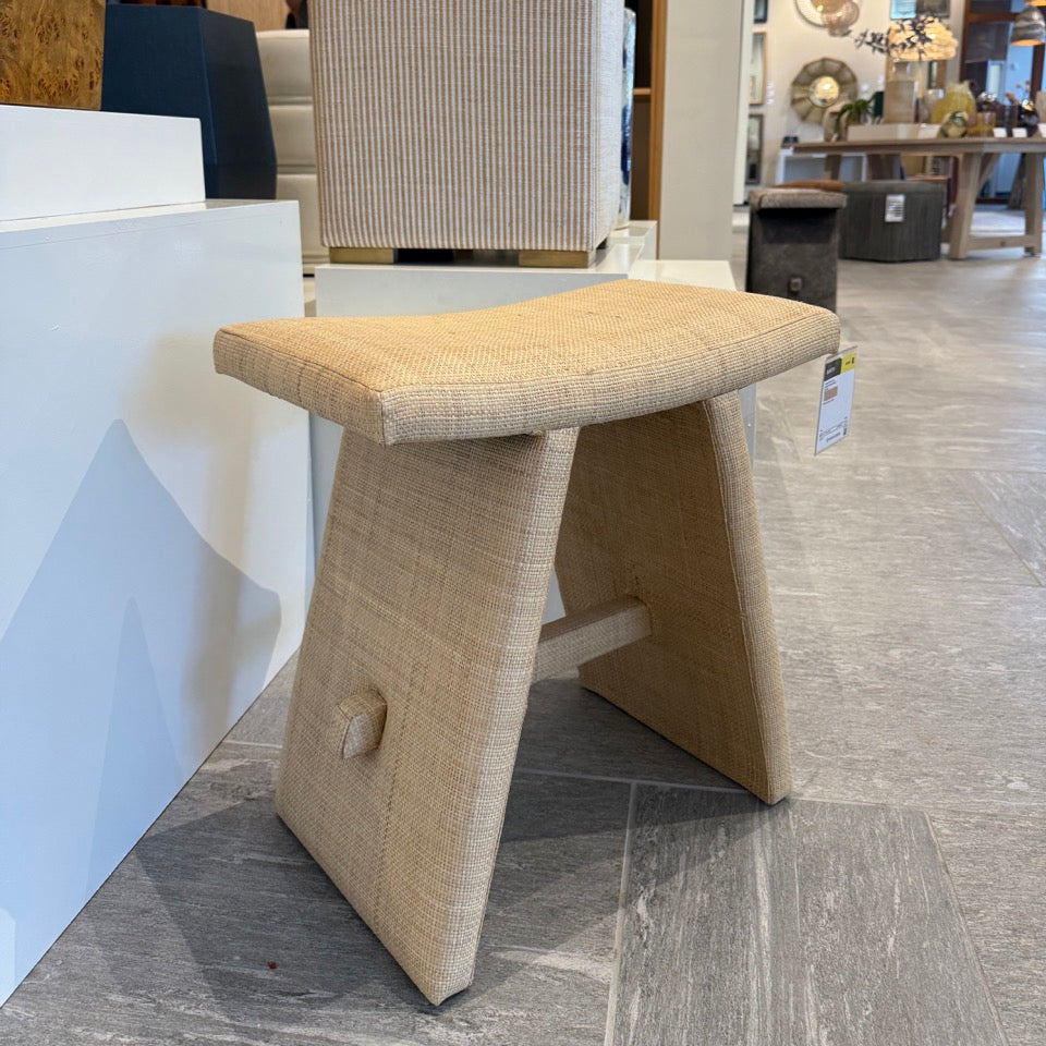 Beige textured stool in a store setting with furniture and decor items in the background.