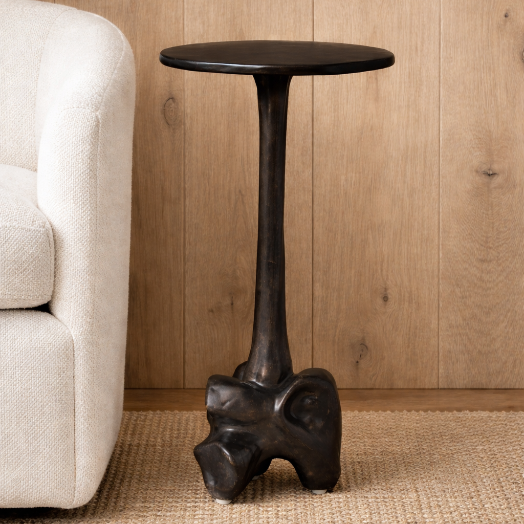 Black side table with abstract design in a room with beige sofa and wooden wall.