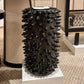 Black spiked decorative vase on a pedestal in an indoor setting with furniture.