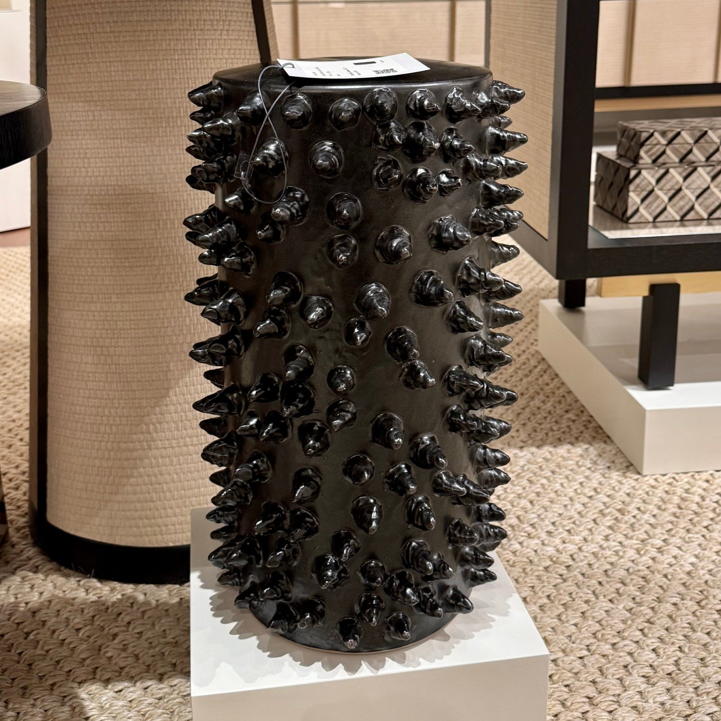 Black spiked decorative vase on a pedestal in an indoor setting with furniture.