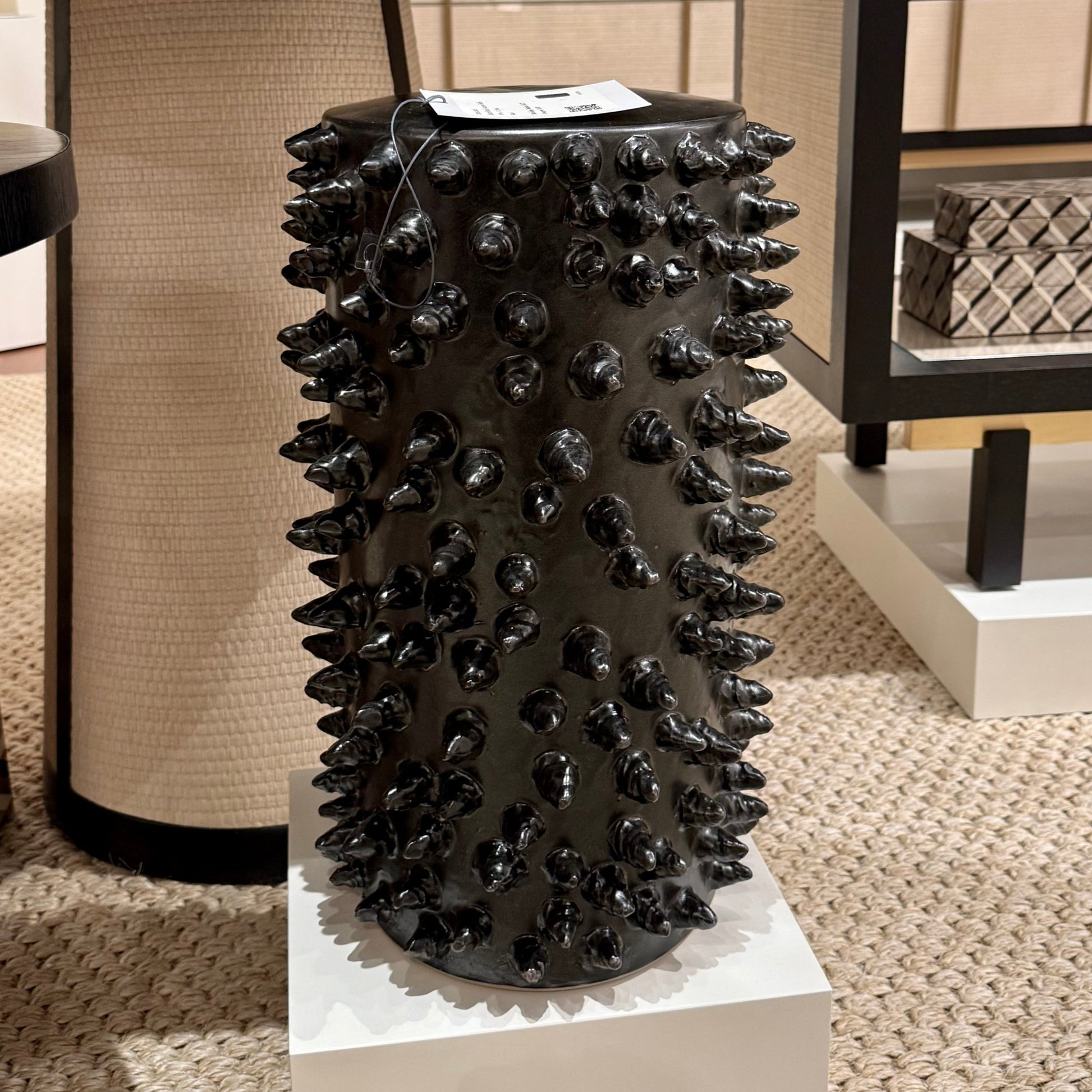 Black spiked decorative vase on a pedestal in an indoor setting with furniture.