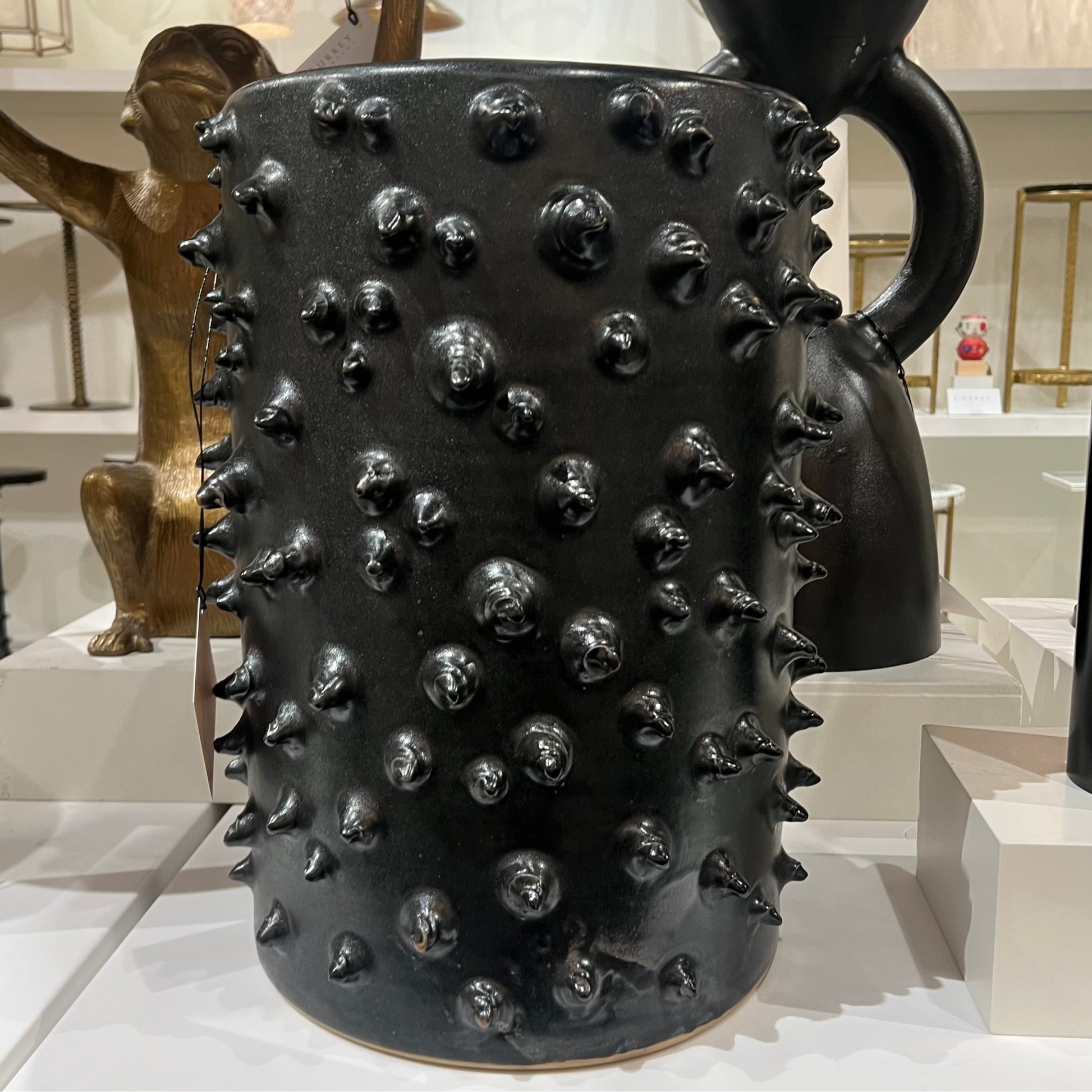 Black ceramic pitcher with spiky texture in a showroom setting