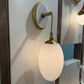 Wall-mounted lamp with white shade and gold fixture on a white surface.
