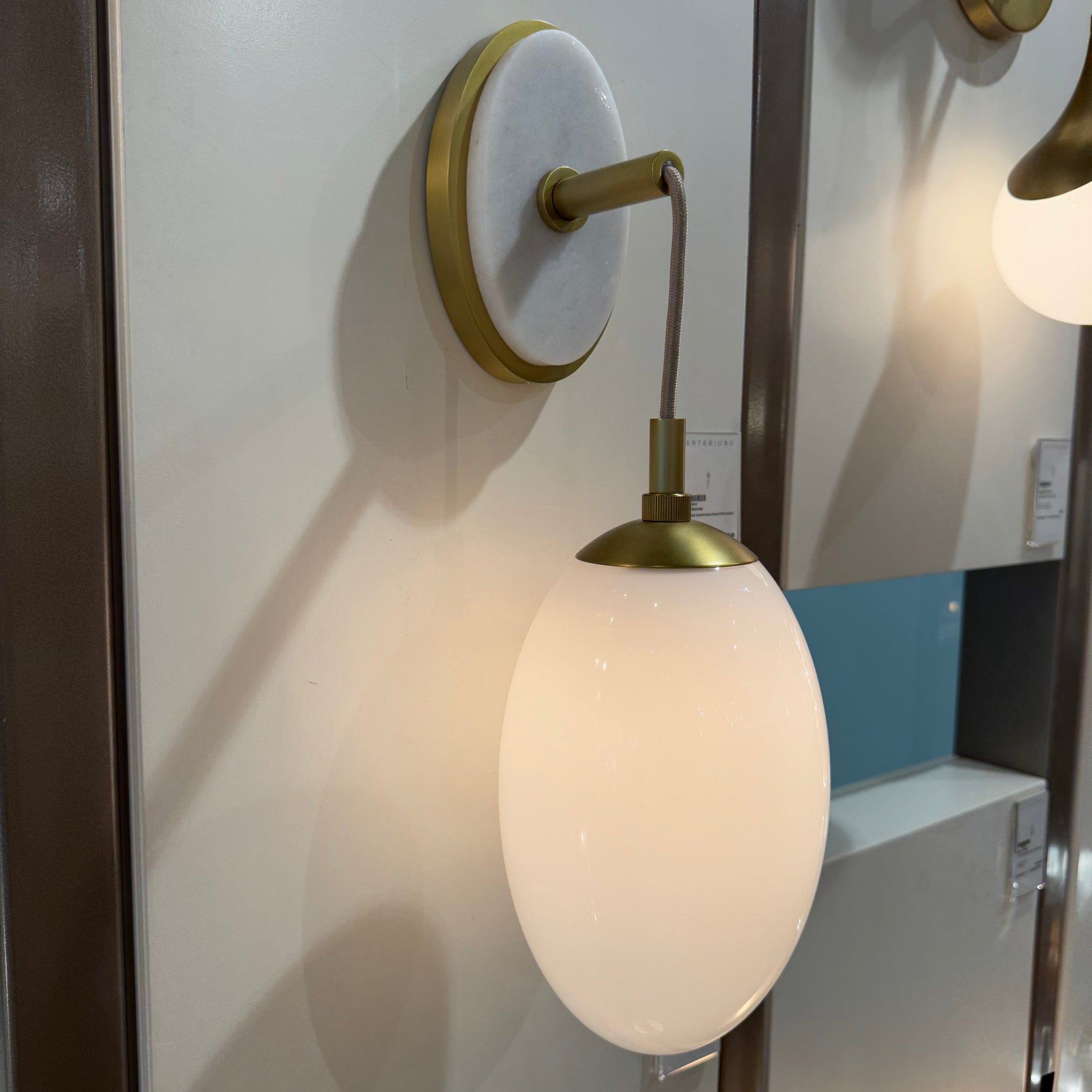 Wall-mounted lamp with white shade and gold fixture on a white surface.