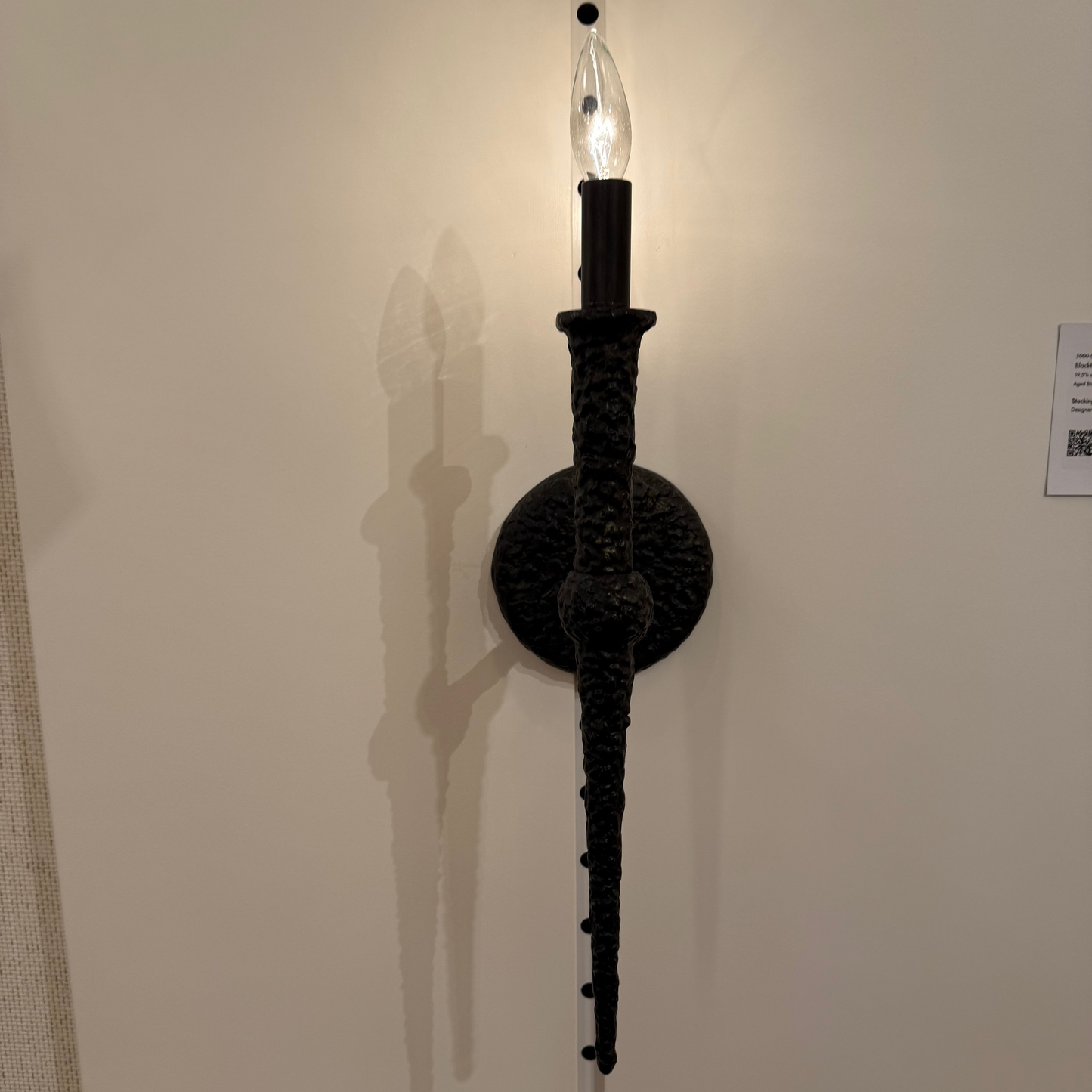 Decorative wall sconce with a long arm on a plain wall.