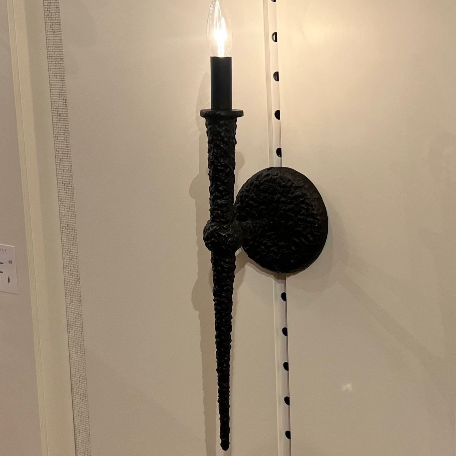 Wall-mounted candle holder with a black finish on a white wall.