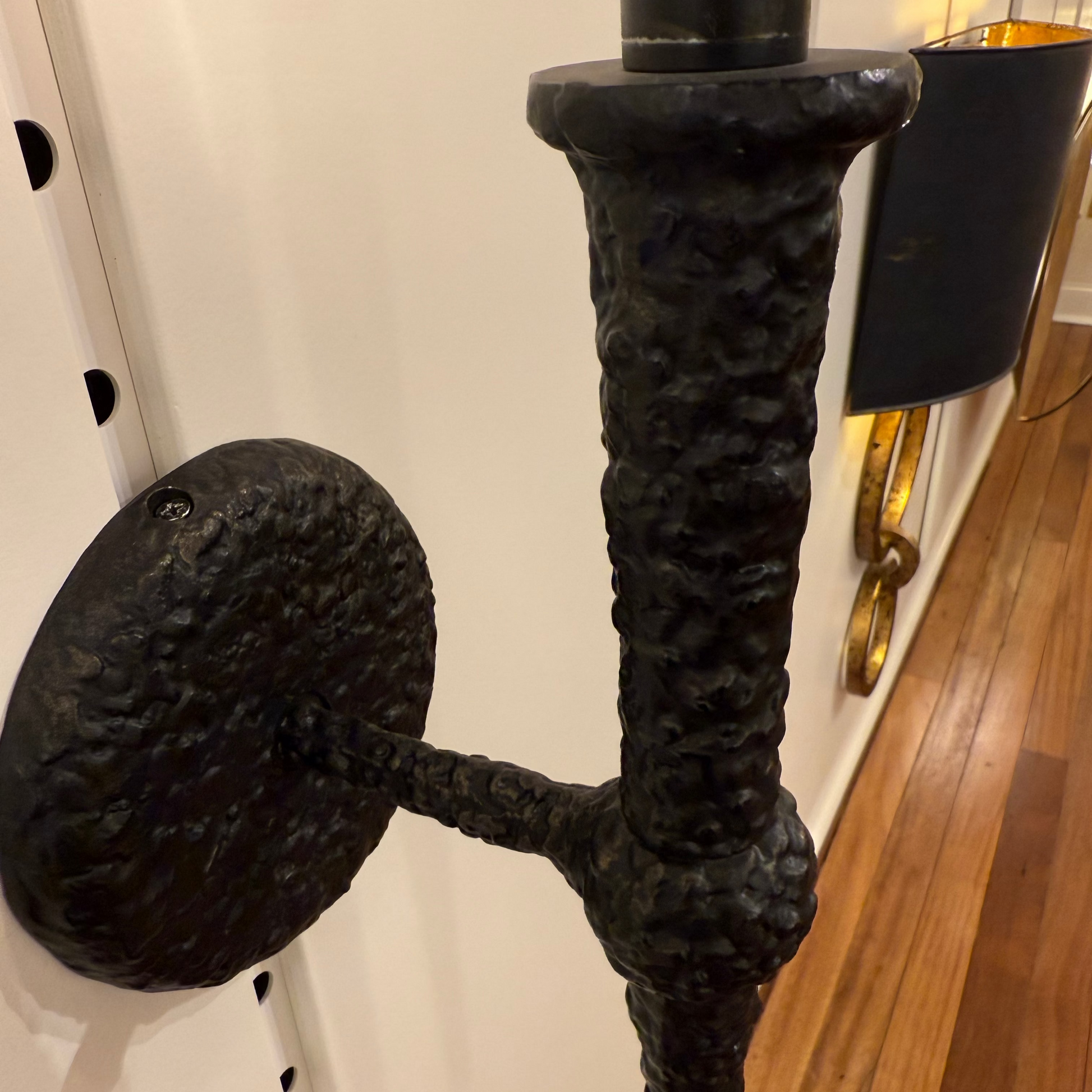 Decorative black metal wall sconce with a textured finish on a wooden floor.