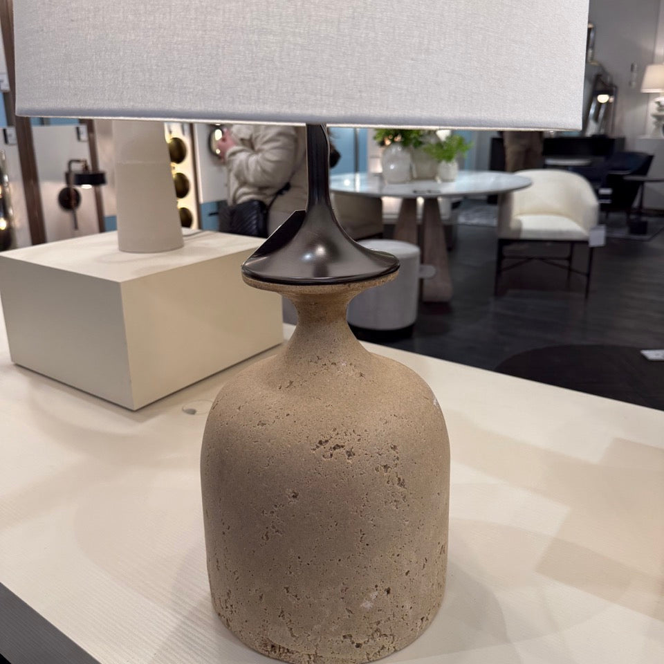Table lamp with a textured base and white shade on a table in an indoor setting.