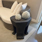 Black side table with decorative items next to a white sofa in a living room setting.