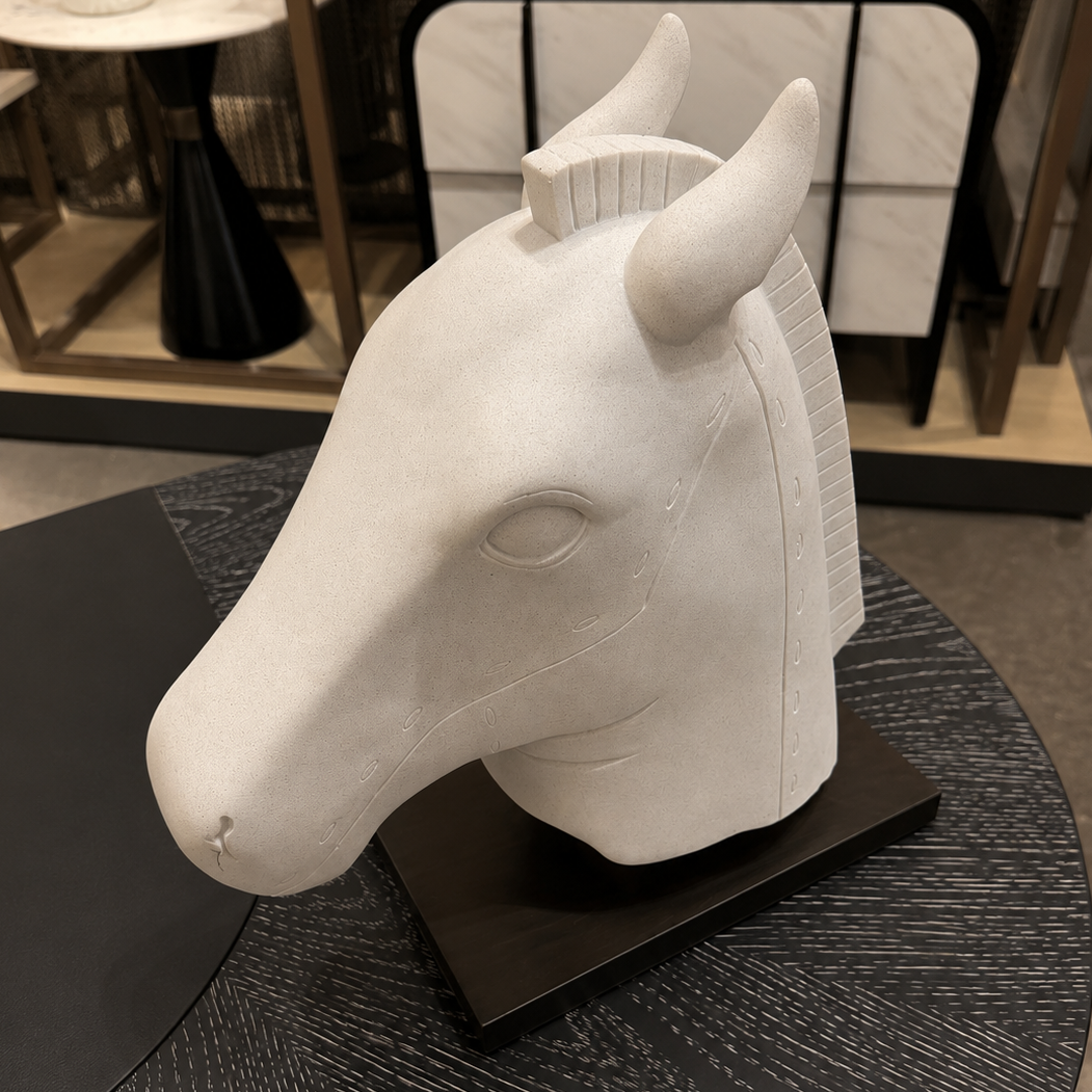 A white sculptural horse head bust displayed on a black rectangular base, set on a dark round table in an indoor showroom environment.