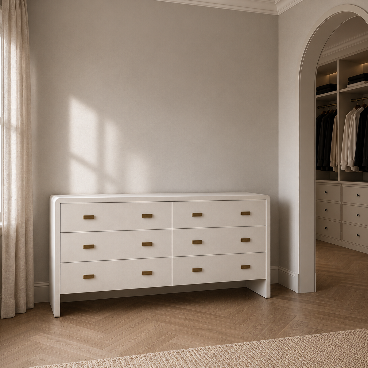 A white wooden dresser with six drawers and small brass handles, positioned against a neutral gray wall in a styled bedroom or dressing area with wood flooring and an arched doorway leading to a closet.