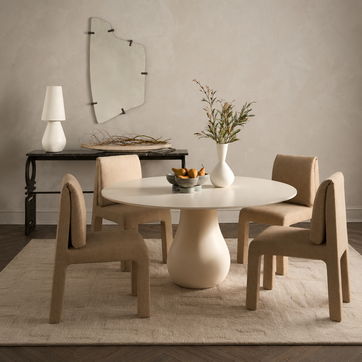 A round dining table with a sculptural pedestal base and four upholstered chairs in a warm neutral dining room setting.