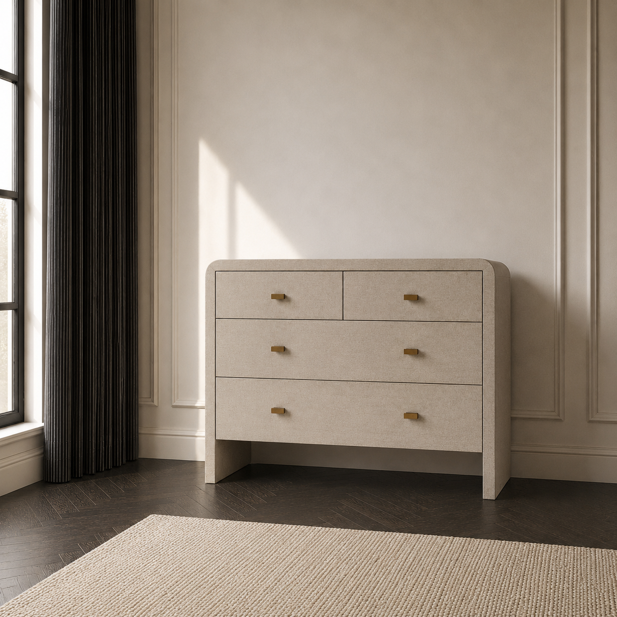 Sand faux shagreen chest of drawers with brass handles, styled in a modern bedroom setting with dark wood flooring, a textured rug, and a window with dark curtains.