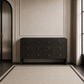 A dark mushroom faux shagreen dresser with six drawers and small brass handles, positioned against a beige wall in a styled room with a textured rug, curtains, and a ribbed glass door.