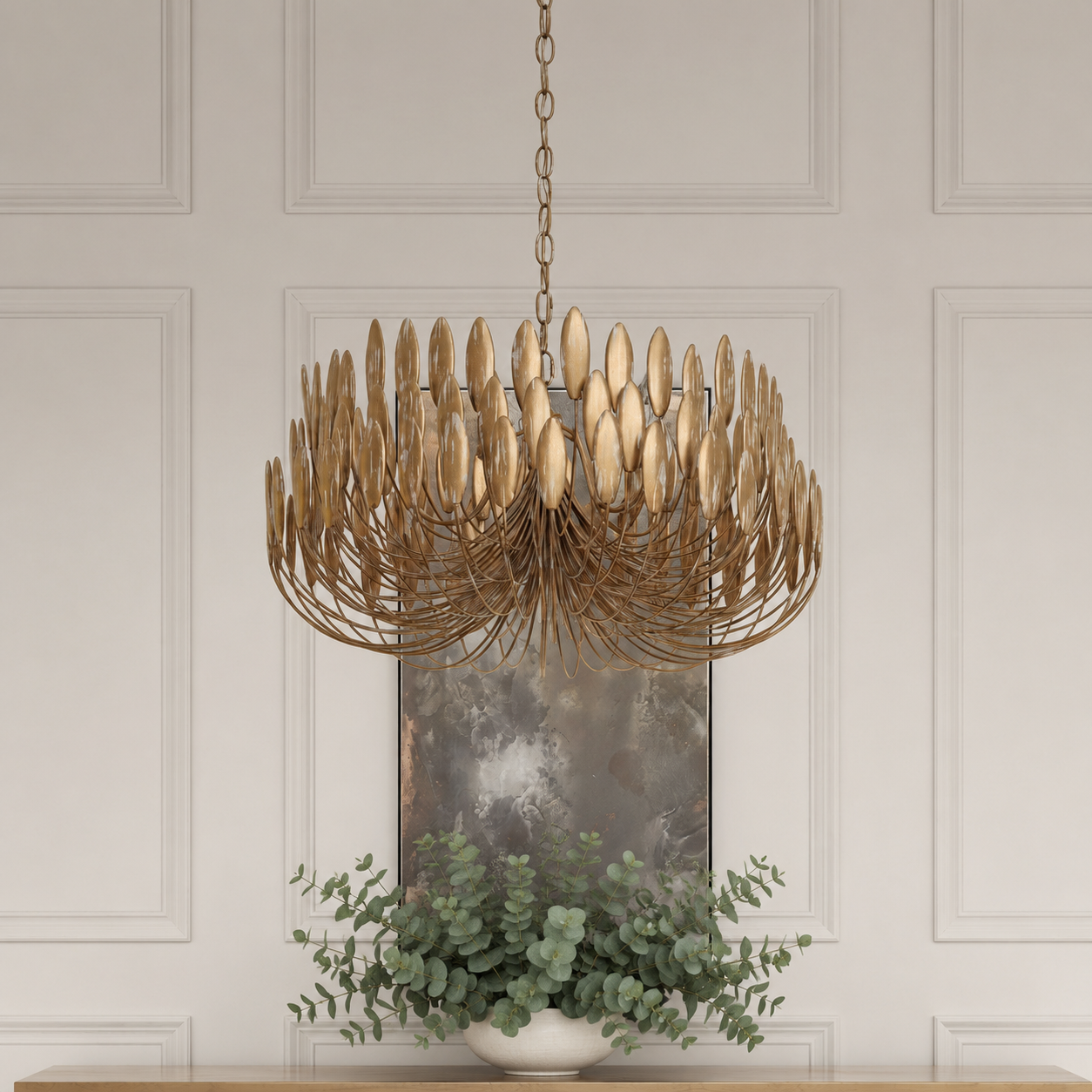 A modern multi-light chandelier with a bronze metal frame and warm gold-toned glass shades, hanging in front of a white paneled wall above a console table with a potted green plant.