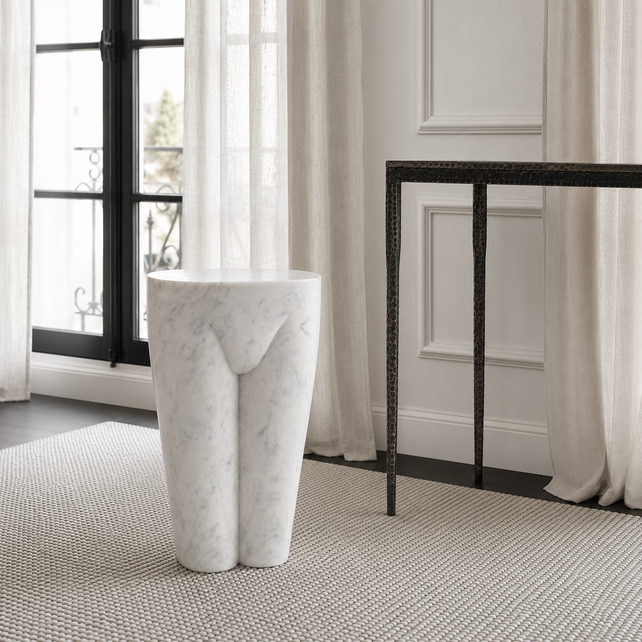 A white marble pedestal shaped like a stylized female torso, set in a modern bathroom or hallway with a woven rug, sheer curtains, and a black metal console table.