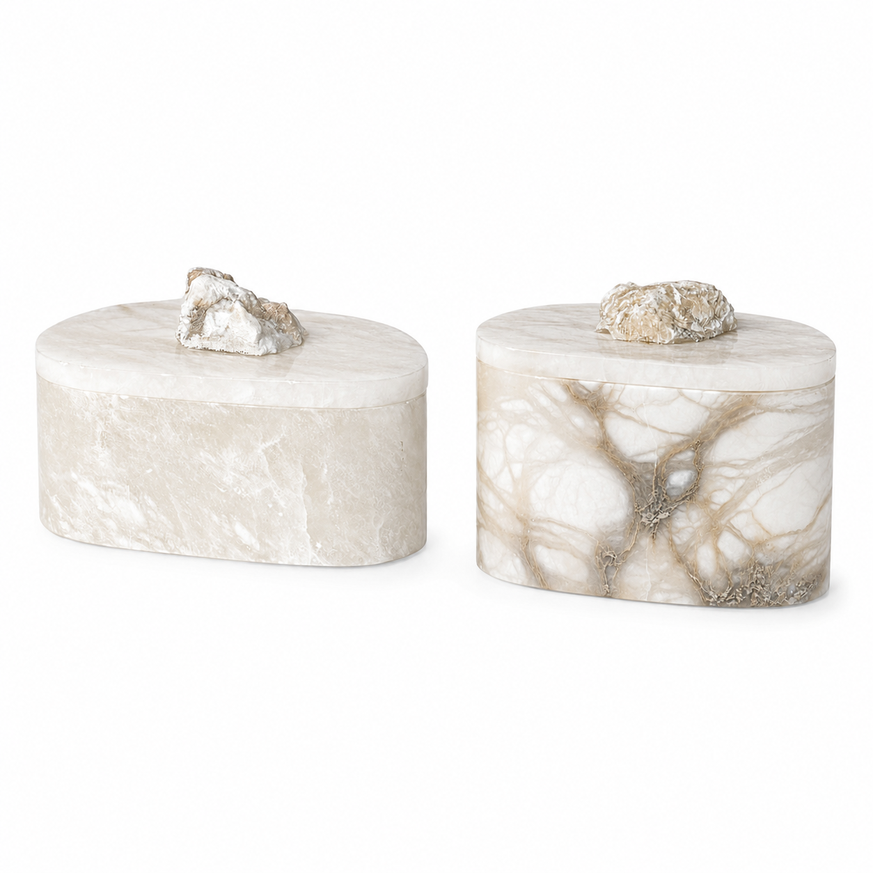 Two oval marble decorative boxes with matching lids, one in light beige marble and one in white marble with tan veining, each topped with a rough natural stone piece, on a white background.